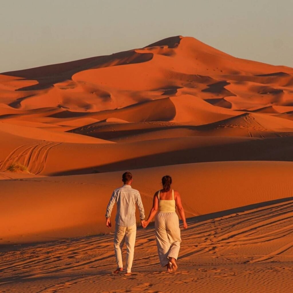 Couple walking hand in hand through the Sahara Desert at sunset on a 5 Days Tour from Marrakech to Fes.