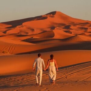 Couple walking hand in hand through the Sahara Desert at sunset on a 5 Days Tour from Marrakech to Fes.